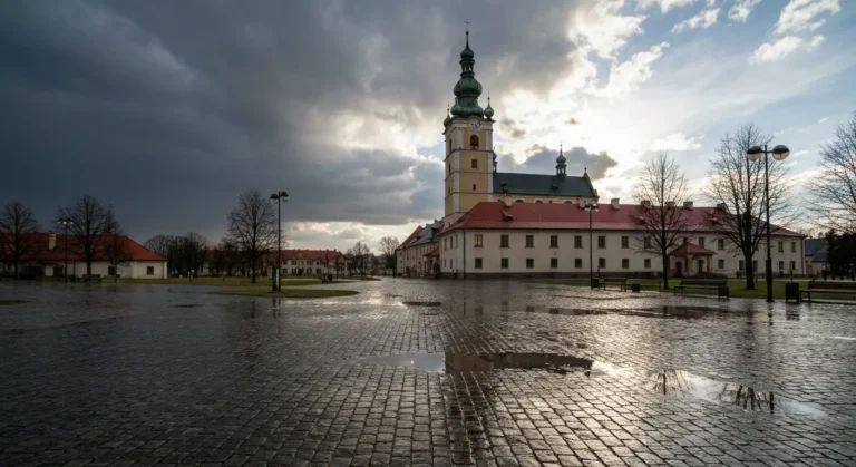 Wieza klasztoru na Jasnej Gorze w Czestochowie pod ciemnymi chmurami deszczowymi, mokry bruk alei odbijajacy swiatlo po